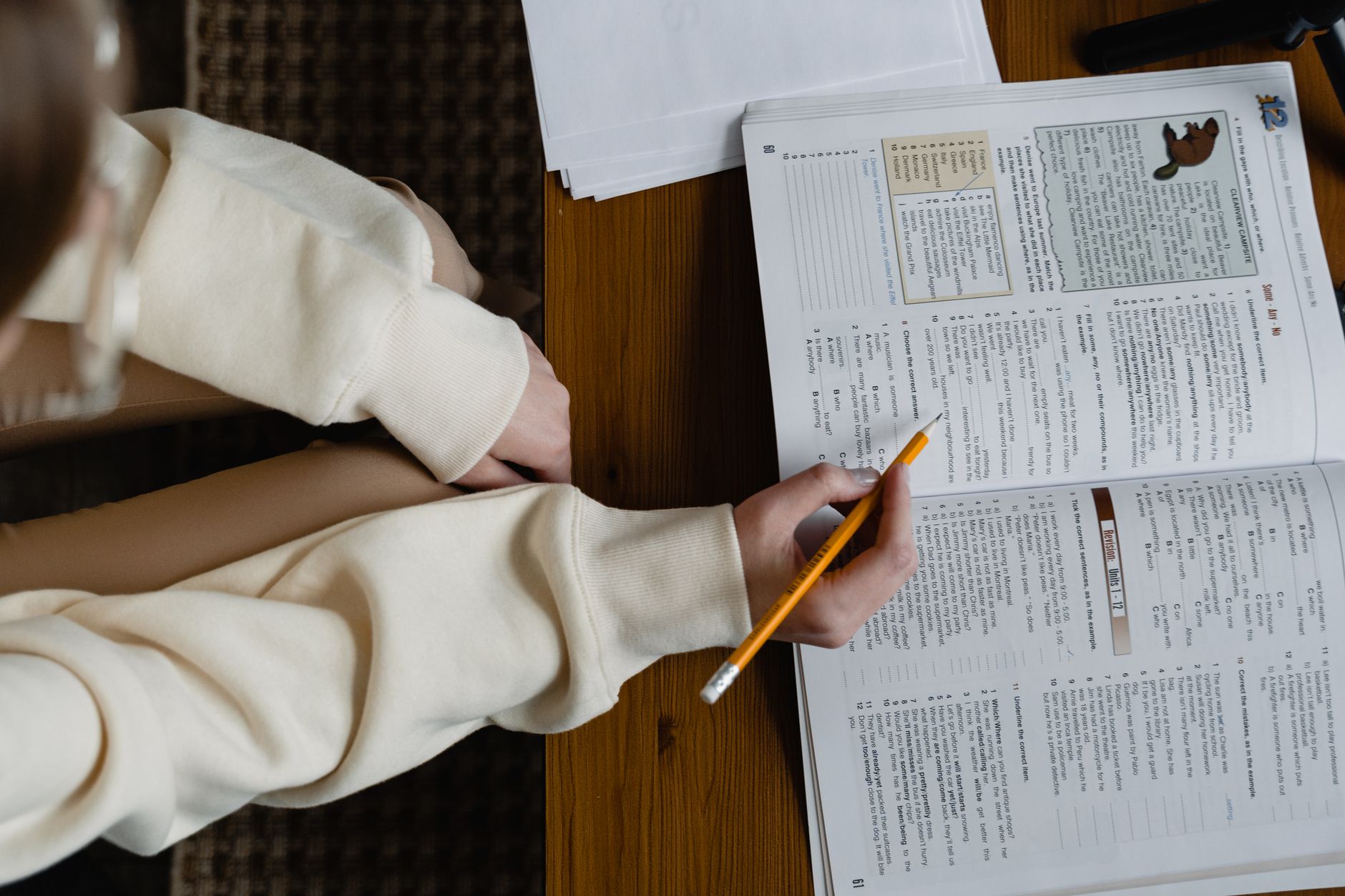 person holding a pencil in front of an open book on table